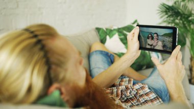 Genç adam evde kanepe yalan tablet bilgisayar kullanarak arkadaşlarınızla sohbet sakallı