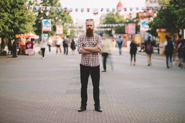 Young bearded man standing still at sidewalk in crowd traffic with people moving around