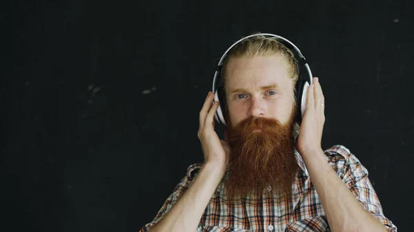 Portret zbliżenie Brodaty mężczyzna młody słuchawki słuchać muzyki i patrząc na kamery uśmiechający się — Zdjęcie stockowe