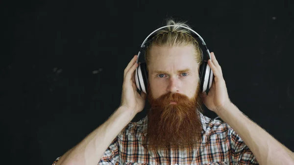 Portrait rapproché de jeune homme barbu dans les écouteurs écouter de la musique et regarder dans la caméra souriant — Photo