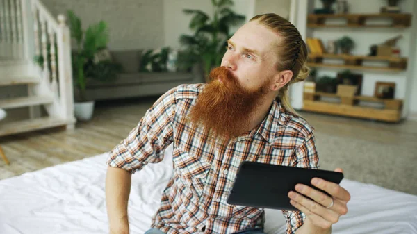 Jovem barbudo usando tablet computador ter vídeo chat sentado na cama em casa — Fotografia de Stock