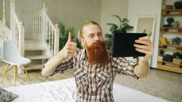 Jovem barbudo usando tablet computador ter vídeo chat sentado na cama em casa — Fotografia de Stock