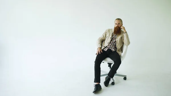Komoly szakállas ember ül irodai forgószék, és vizsgálja a fényképezőgép fehér háttér — Stock Fotó