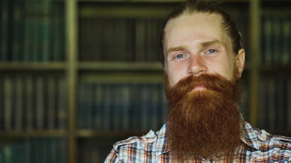 Nahaufnahme Porträt eines jungen bärtigen Mannes, der in der Bibliothek glücklich lächelt und in die Kamera blickt — Stockfoto