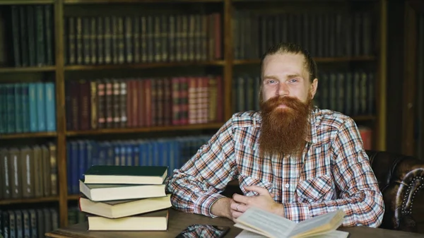 Retrato jovem barbudo homem sorrindo feliz na biblioteca e olhando para a câmera — Fotografia de Stock