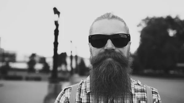 Retrato de hombre turista barbudo hipster en gafas de sol mirando a la cámara y sonriendo al fondo de la ciudad —  Fotos de Stock