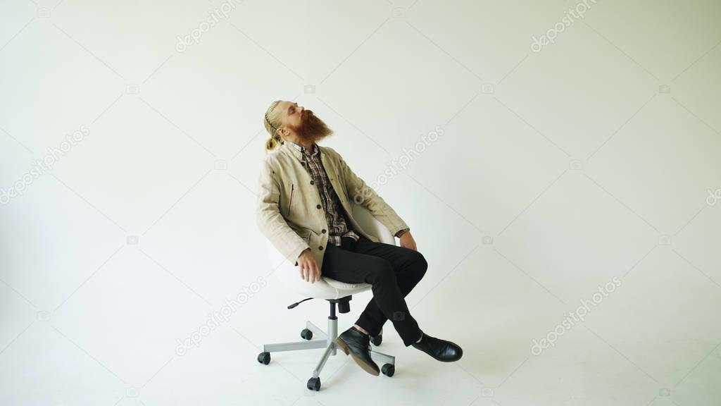 Boring bearded man turning on swivel office chair on white background