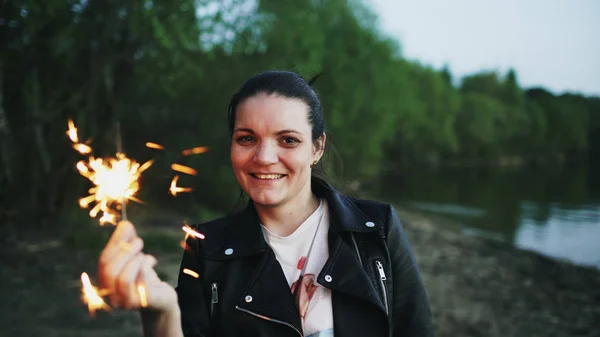 Portrait of young smiling woman with sparkler celebrating at beach party — Stock Photo, Image