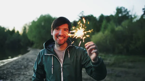 Ritratto di giovane uomo sorridente con sparkler che festeggia alla festa in spiaggia — Foto Stock