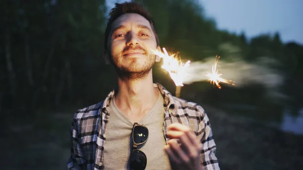 Portrait of young smiling man with sparkler celebrating at beach party — Stock Photo, Image