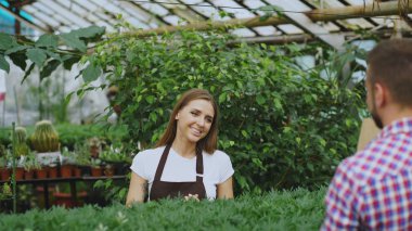 Genç gülümseyen satıcı çiçekçi Bahçe merkezinde çalışıyor. Kadın müşteri mağazasında alışveriş çantası sağlar