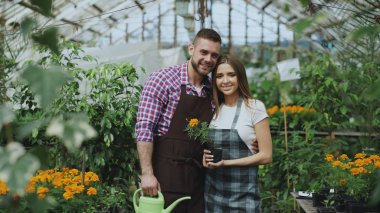 Serada gülümseyen mutlu genç bir çift. Bahçe kameraya bakarak önlük çekici kadın ve adam çiçekçi iş