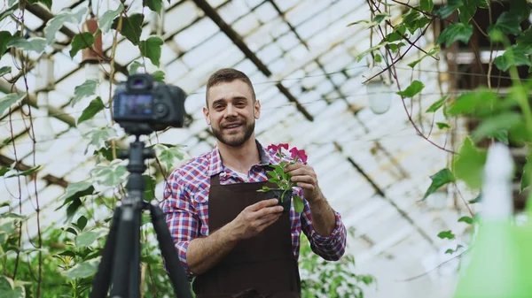 Young smiling blogger man florist in apron holding flower talking and recording video blog for his online vlog about gardening