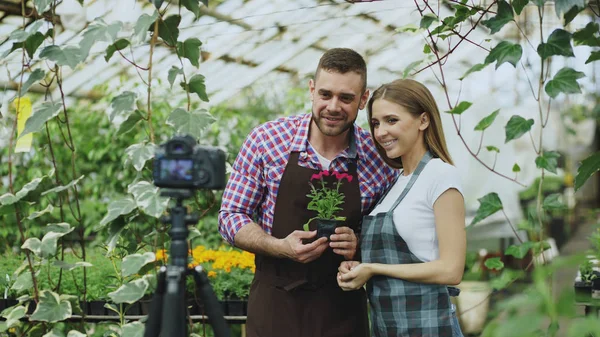 Νεαρός χαμογελαστό blogger ζευγάρι κηπουροί στην ποδιά κρατώντας λουλούδι μιλάμε και την καταγραφή βίντεο blog για online vlog για κηπουρική — Φωτογραφία Αρχείου