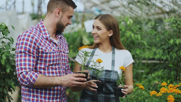 Joven florista mujer amigable hablando con el cliente y dándole consejos mientras trabaja en el centro de jardín —  Fotos de Stock
