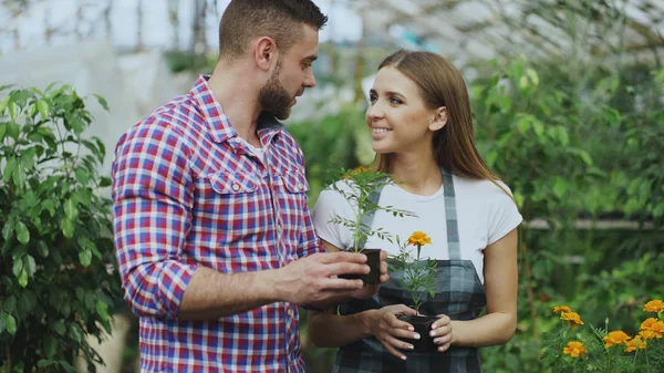 Young friendly woman florist talking to customer and giving him advice while working in garden center — Stock Photo, Image