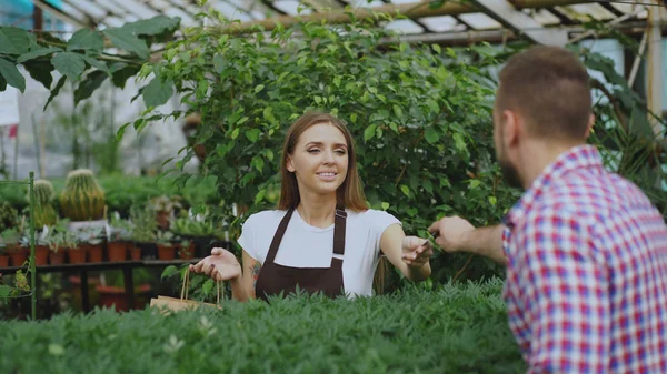 Młodych uśmiechający się sprzedawca kwiaciarni pracy w centrum ogrodowym. Kobieta daje torba na zakupy do klienta i Dokonywanie płatności kartą kredytową w sklepie — Zdjęcie stockowe