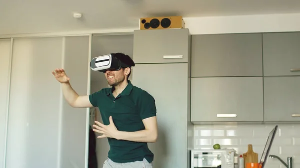 Смішний молодий чоловік у віртуальній реальності 360 гарнітура танцює на кухні вранці, слухаючи музику і розважаючись вдома — стокове фото