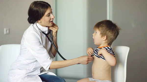 Mladá žena doktor poslouchá malého chlapce s stetoskop v ordinaci — Stock fotografie