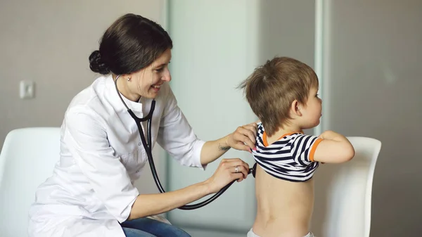 Mladá žena doktor mluví malého chlapce a poslech stetoskopem v ordinaci — Stock fotografie