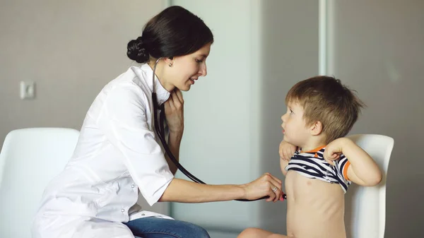 Mladá žena doktor mluví malého chlapce a poslech stetoskopem v ordinaci — Stock fotografie