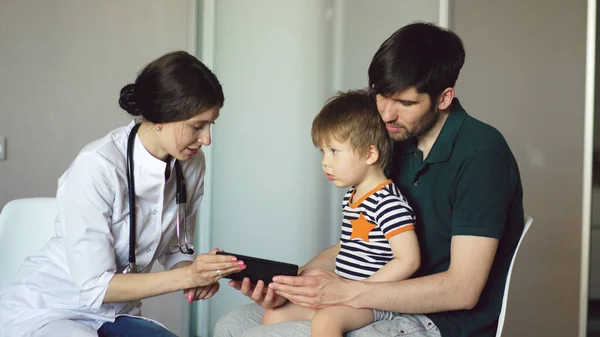 Mladá žena doktor mluvil s otcem malého chlapce pomocí tabletového počítače v ordinaci — Stock fotografie