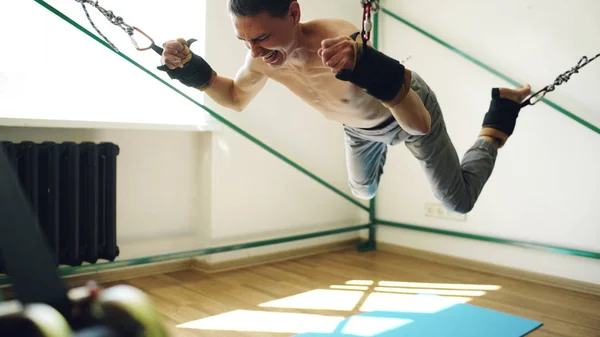 Молодой человек делает упражнения на четвертование оборудования для йоги и тянет свои руки и ноги веревками — стоковое фото