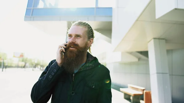 Jovem barbudo hipster homem concentrado falando no telefone na cidaderua, conversa perto de prédio de escritórios — Fotografia de Stock