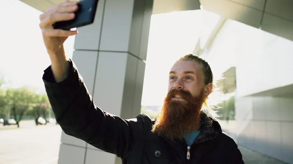 Jovem homem hipster barbudo tirar foto selfie usando câmera de smartphone ao ar livre na rua da cidade — Fotografia de Stock
