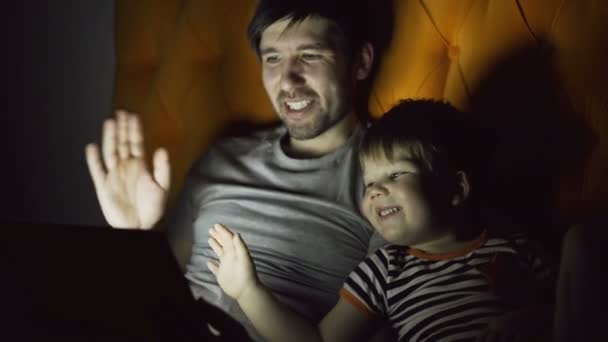 Kärleksfull Fader och hans lille son med online video-chat med morföräldrar använda Tablet PC: n och liggandes i sängen i kväll hemma — Stockvideo