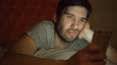 Yakın çekim sıkılmış gencin internet bağımlılığı ve uykusuzluk geceleri evde yatakta yatan smartphone kullanarak sahip