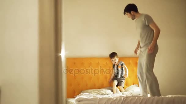 Padre feliz con el pequeño hijo bailando y divertirse en la cama en casa por la noche antes de acostarse — Vídeos de Stock