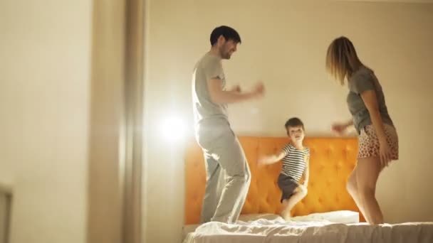 Família feliz com o pequeno filho dançando e se divertir na cama em casa à noite antes de dormir — Vídeo de Stock