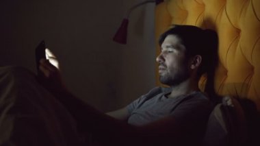 Uyumadan önce evde yatakta yatan sörf sosyal medya için tablet bilgisayar kullanan genç gülümseyen adam