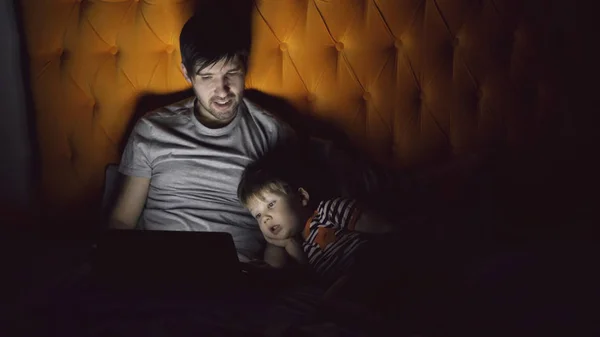Fiatal apa és a fia kis rajzfilm film tabletta számítógépet használ, és az este otthon az ágyban fekve beszélt — Stock Fotó