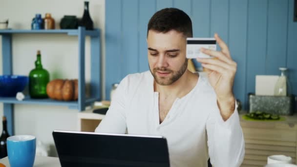 Evde mutfakta kahvaltı var genç adam Online kullanarak kredi kartı ve dizüstü bilgisayar alışveriş sahip — Stok video