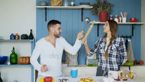 Glückliches Paar, das in der Küche mit Schöpfkelle und Nudelholz kämpft, während es zu Hause frühstückt — Stockvideo