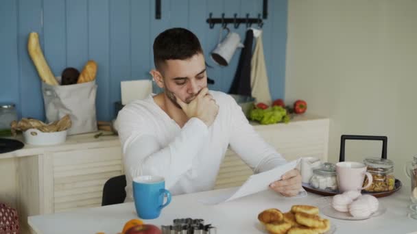 Verärgerter junger Mann liest Brief mit unbezahlter Rechnung in der Küche zu Hause — Stockvideo