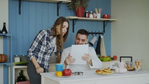 Aantrekkelijke gelukkige paar goede ontvouwen nieuwsbrief ontvangen in de keuken tijdje thuis ontbijten — Stockvideo