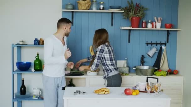 Junge fröhliche Paare haben Spaß beim Tanzen und Singen, während sie zu Hause den Tisch zum Frühstück in der Küche decken — Stockvideo