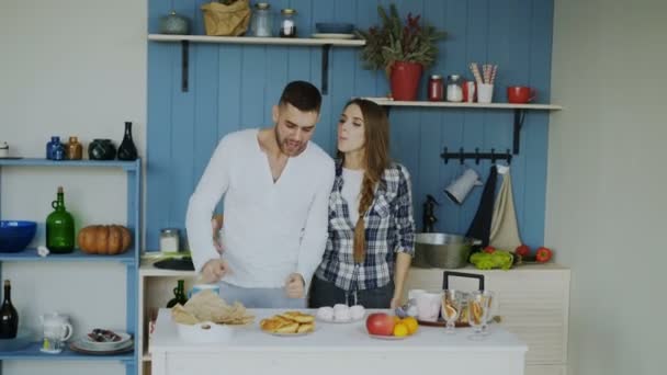 Junge fröhliche Paare haben Spaß beim Tanzen und Singen, während sie zu Hause den Tisch zum Frühstück in der Küche decken — Stockvideo