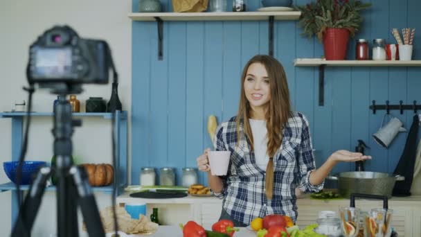 Jovem mulher atraente gravação de vídeo blog de alimentos sobre cozinhar na câmera dslr na cozinha — Vídeo de Stock