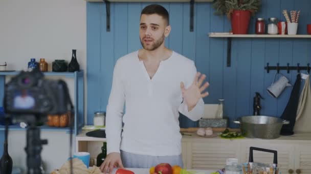 Bonito homem alegre gravação vídeo comida blog sobre cozinhar na câmera dslr na cozinha em casa — Vídeo de Stock