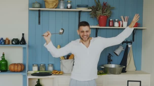 欢快的年轻滑稽的慢动作的人跳舞和唱歌与钢包在厨房做饭在家里 — 图库视频影像
