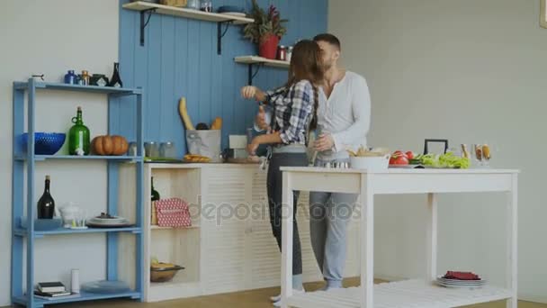 Χαρούμενη και ελκυστικό νεαρό ζευγάρι στην αγάπη χορεύουν μαζί και να διασκεδάσουν στην κουζίνα στο σπίτι για τις διακοπές — Αρχείο Βίντεο