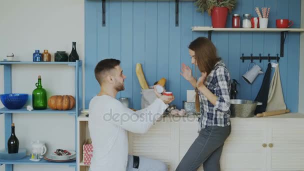 Молодой человек делает предложение своей девушке на кухне дома — стоковое видео