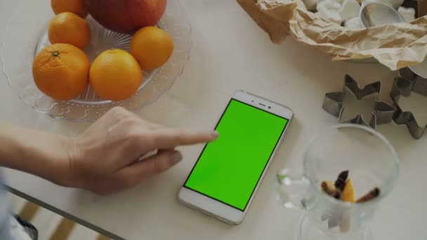 Zbliżenie dłoni womans przeglądania smartfonem z zielonego ekranu na stole w kuchni w domu — Wideo stockowe