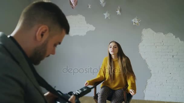 Молодая красивая женщина-модель позирует для фотографа, пока он снимает цифровой камерой в фотостудии в помещении — стоковое видео