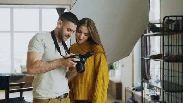 Professionele fotograaf man tonen van foto's op digitale camera aan mooie model meisje in fotostudio binnenshuis — Stockvideo