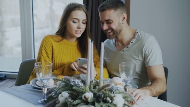 Jonge lachende paar doorbladeren smartphone terwijl het hebben van lunch in café binnen — Stockvideo